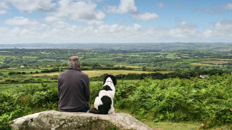 Visitor and their dog sit next to each other on a large rock, enjoying the countryside view